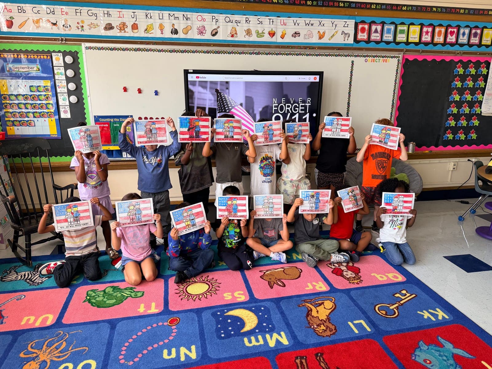 Second-grade students at Madison Elementary hold up their Patriot Day coloring projects during a 9/11 remembrance lesson.