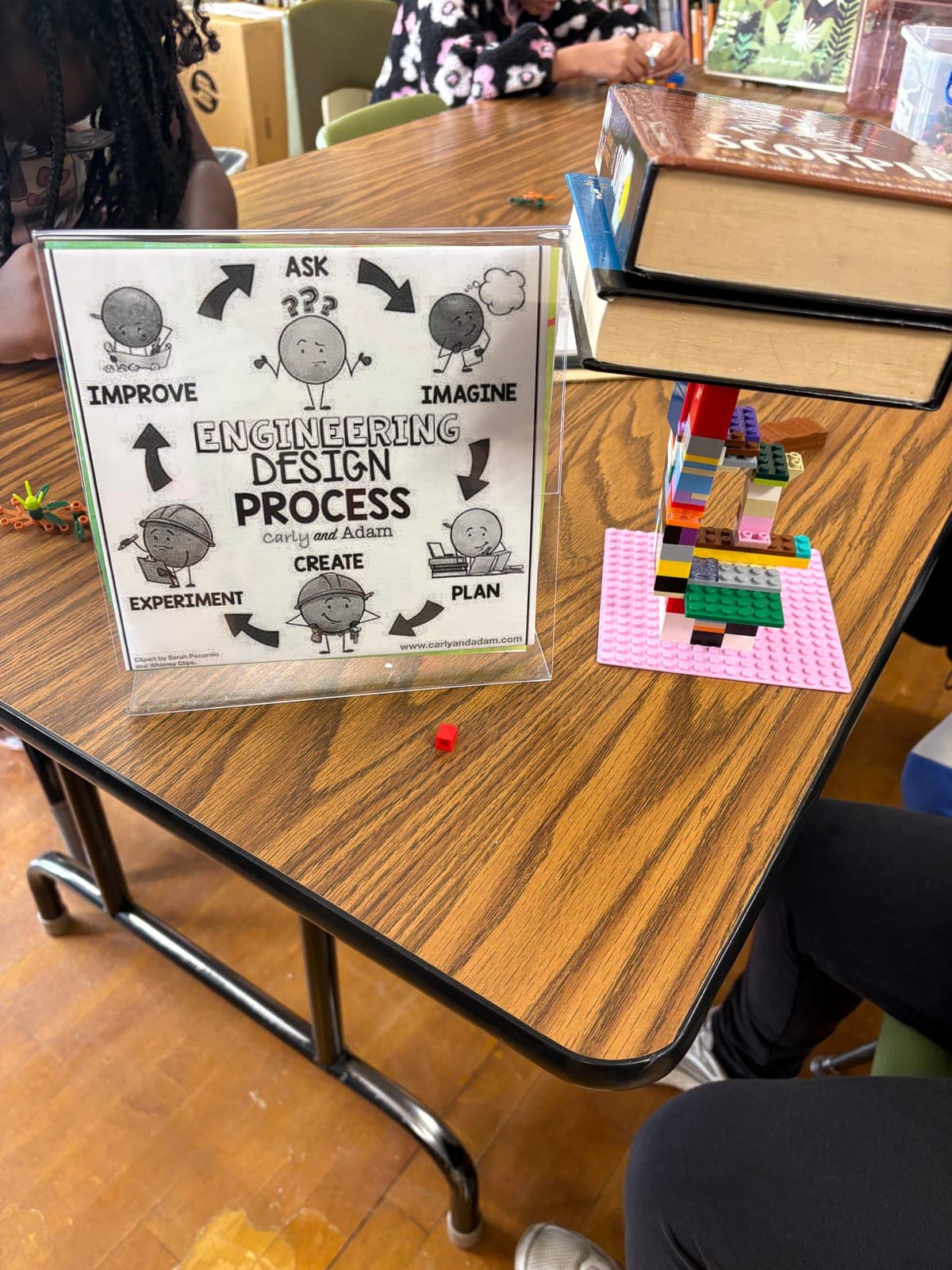 A building-block structure supports books beside an engineering design guide in the school library.